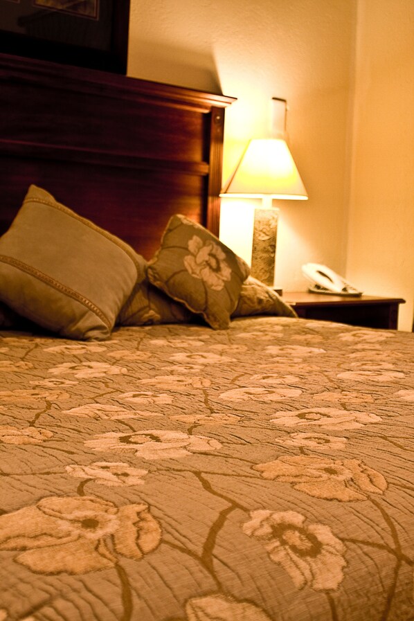 A bed with a floral-patterned bedspread, two pillows, a bedside lamp, and a telephone on a wooden nightstand.
