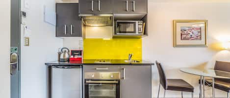 A compact kitchen with a built-in microwave, oven, and a small refrigerator. There is a dining table with chairs and a yellow backsplash.
