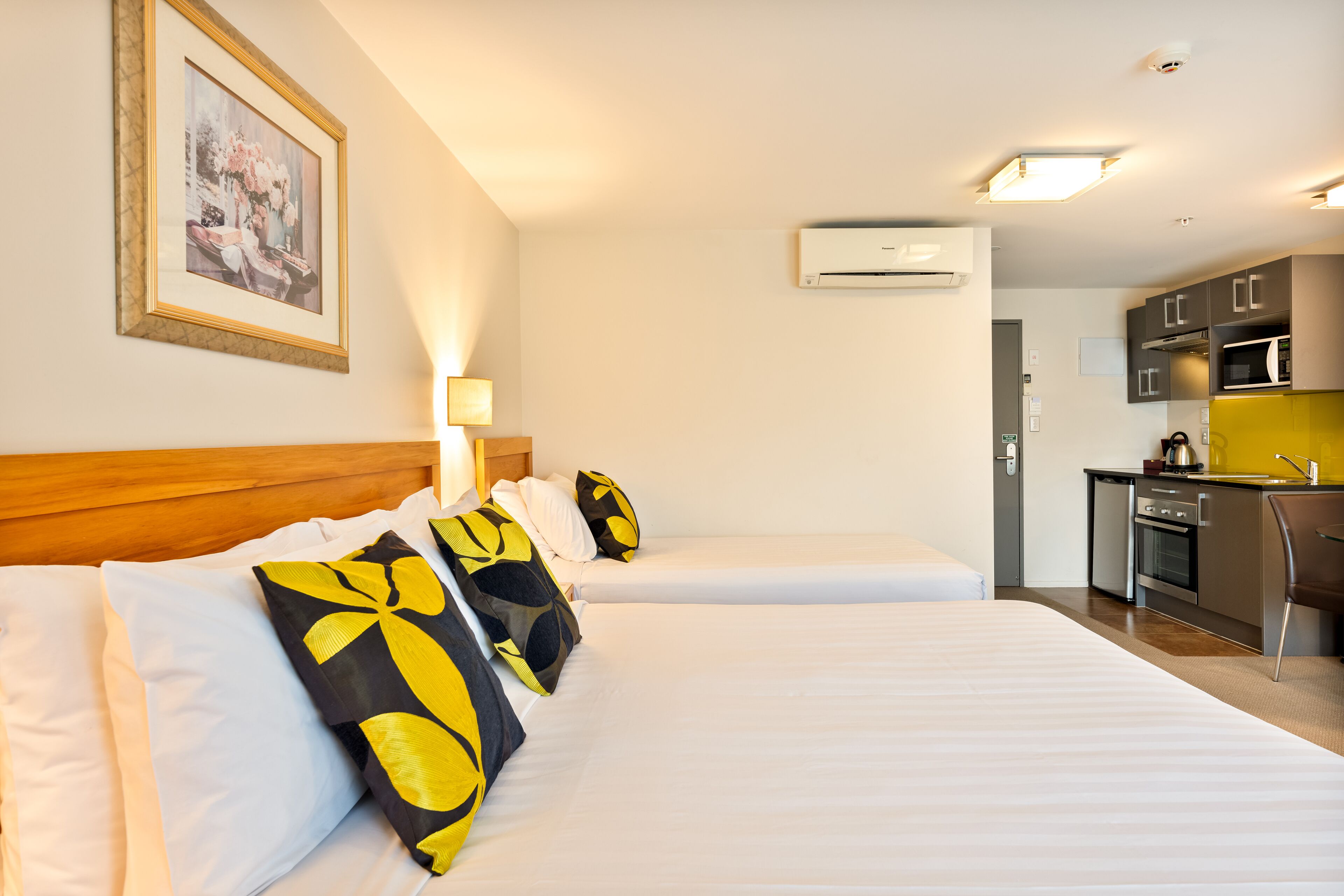 A hotel room with two beds, a kitchenette, and an air conditioning unit.
