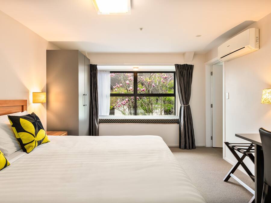 A hotel room with a large bed, a desk, and a window with curtains.