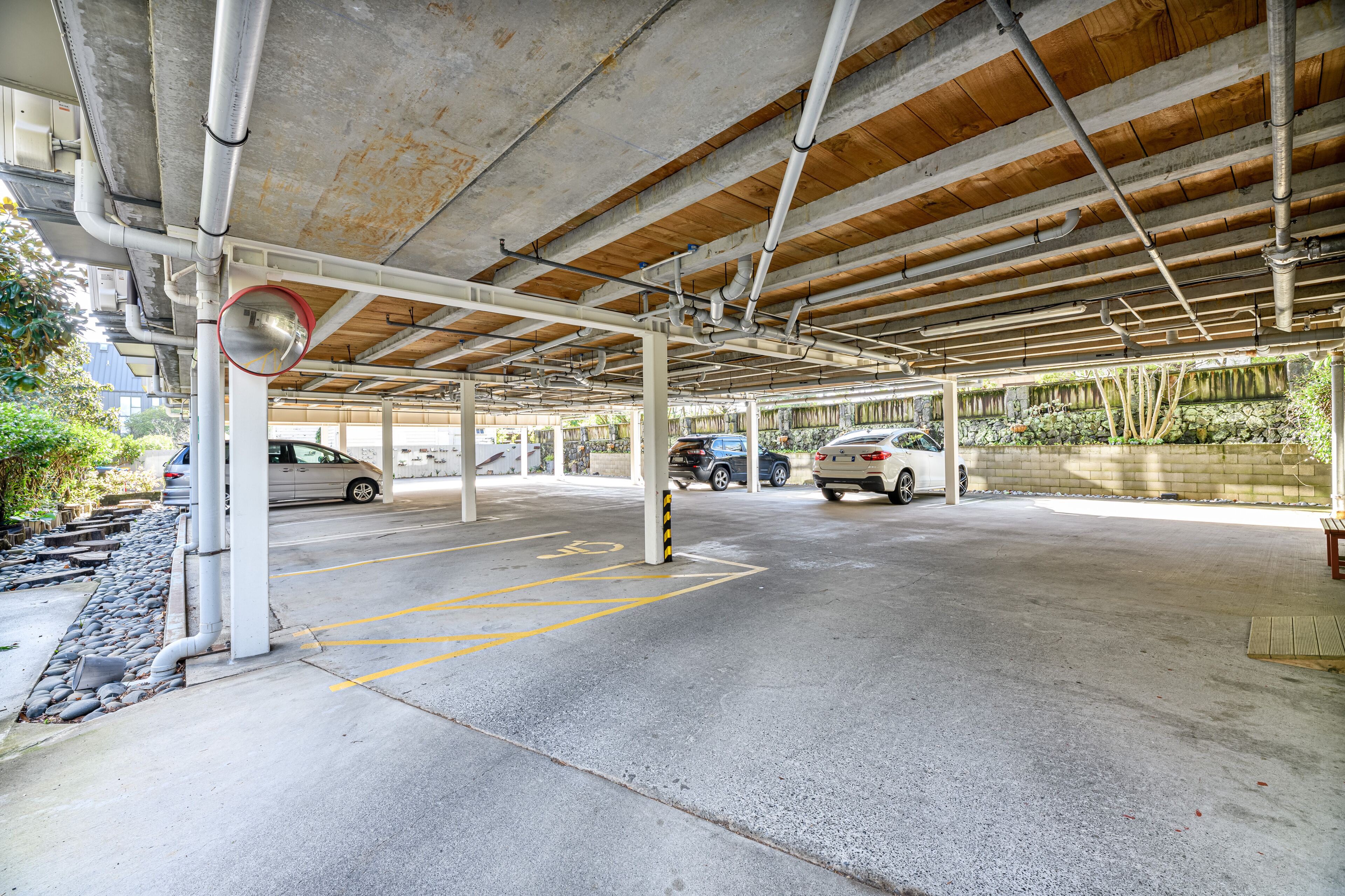 A covered parking area with concrete floors and a wooden ceiling, featuring multiple parking spaces and a visible water drainage system.