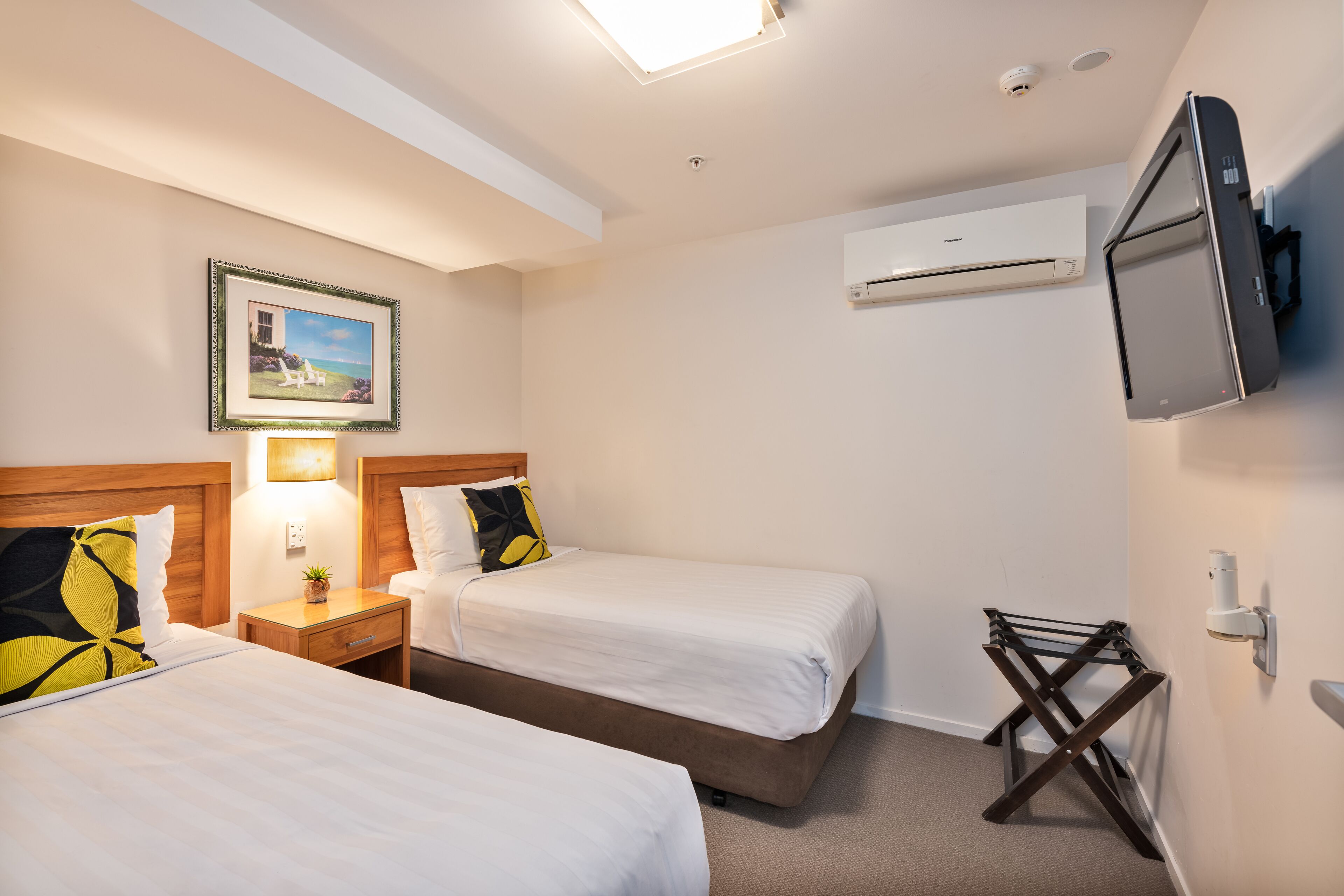A hotel room with two beds, a TV, an air conditioner, and a framed picture on the wall.