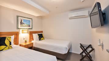 A hotel room with two beds, a TV, an air conditioner, and a framed picture on the wall.