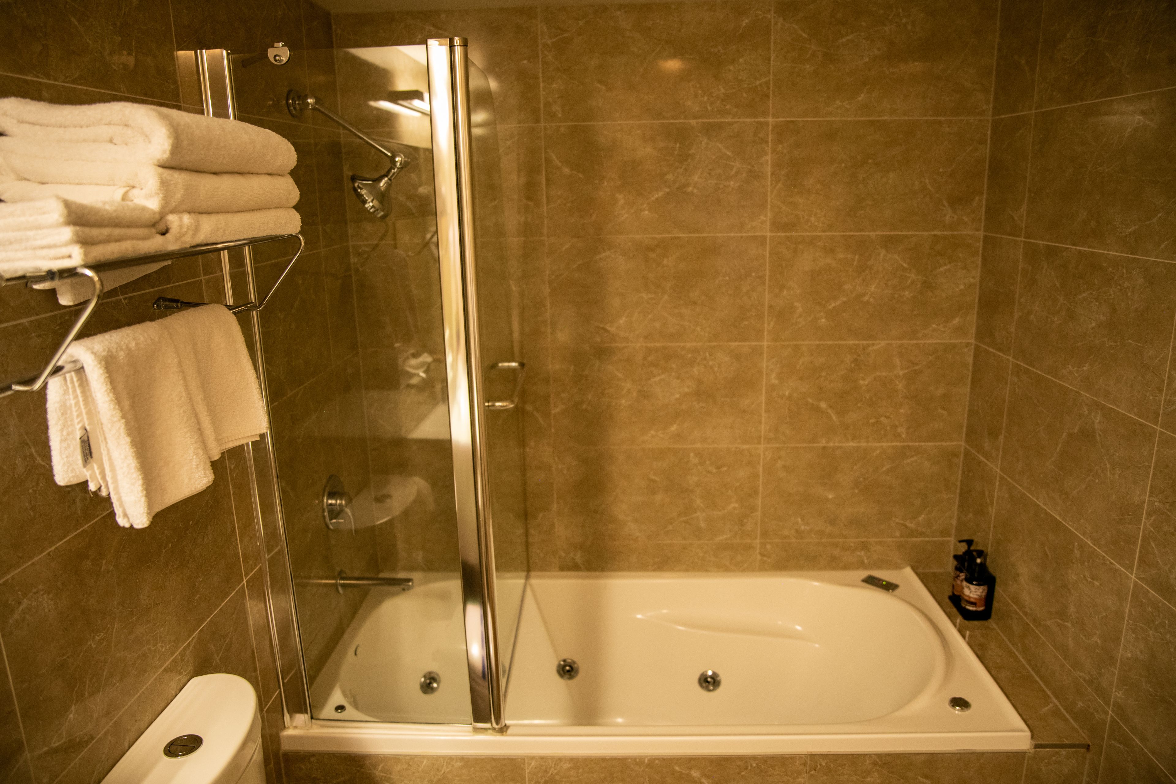 Un baño con bañera, ducha con mampara de vidrio y un perchero con toallas dobladas.