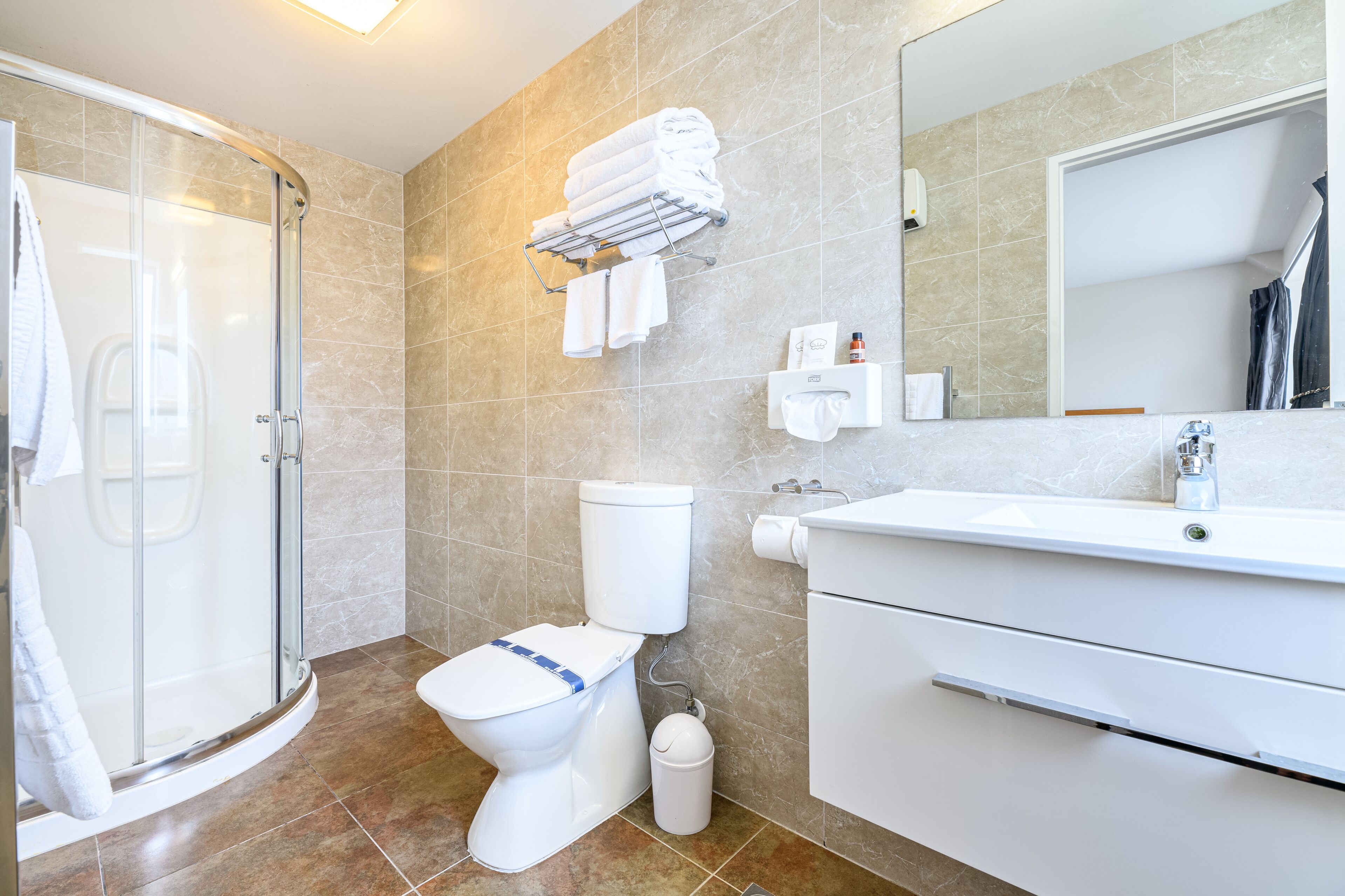 Ein modernes Badezimmer mit Duschkabine aus Glas, Toilette, Waschbecken und Handtuchhalter.