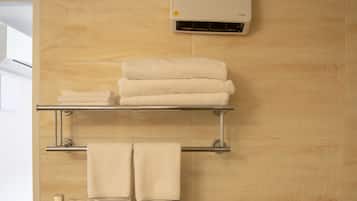 Un baño con toallero, estante con toallas dobladas, dispensador de papel higiénico y aire acondicionado de pared.