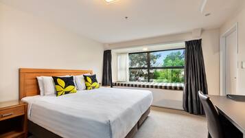 Un dormitorio con cama, escritorio, ventana con cortinas y vista a zonas verdes.
