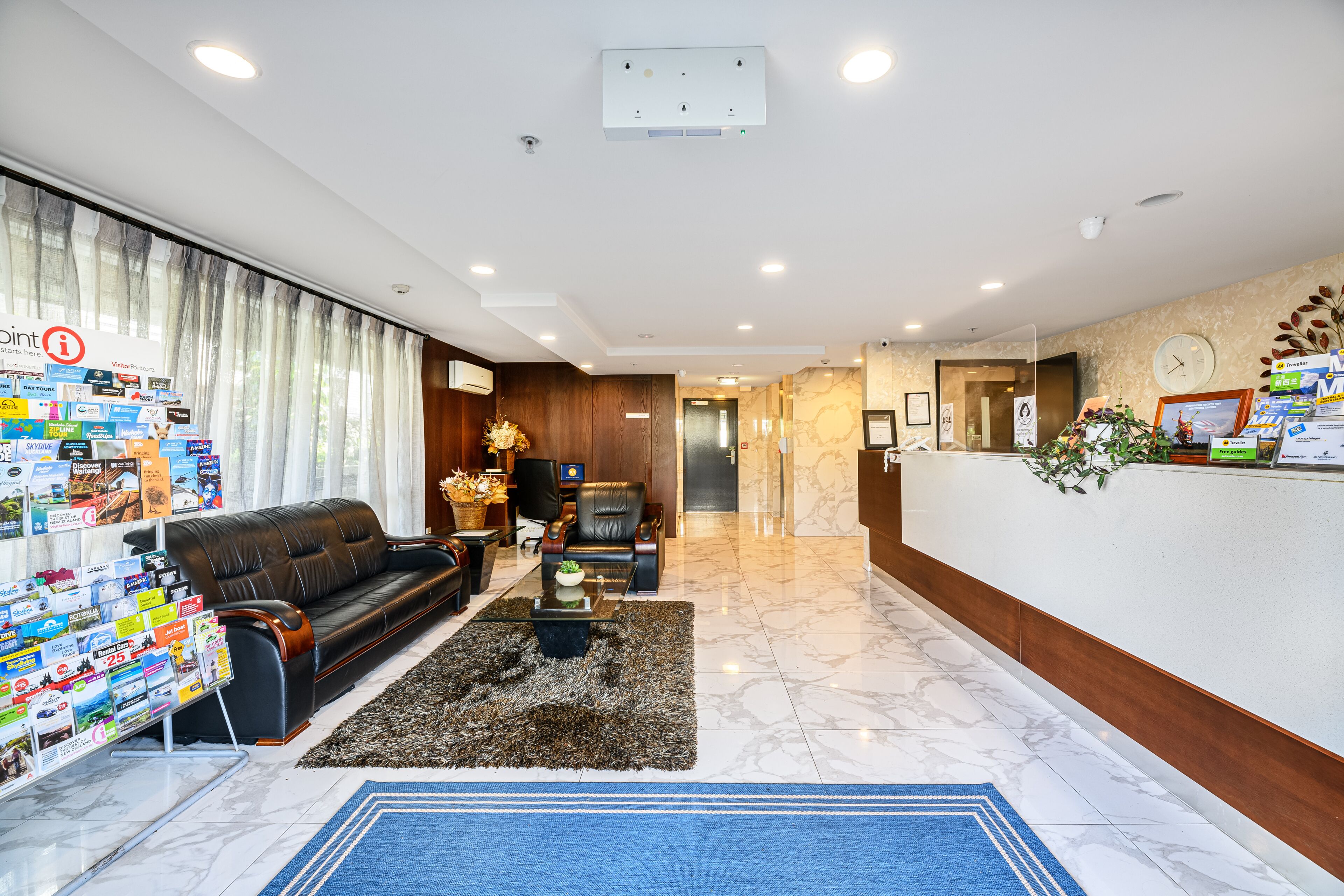 A hotel lobby with a reception desk, a sofa, a coffee table, and a display of magazines.