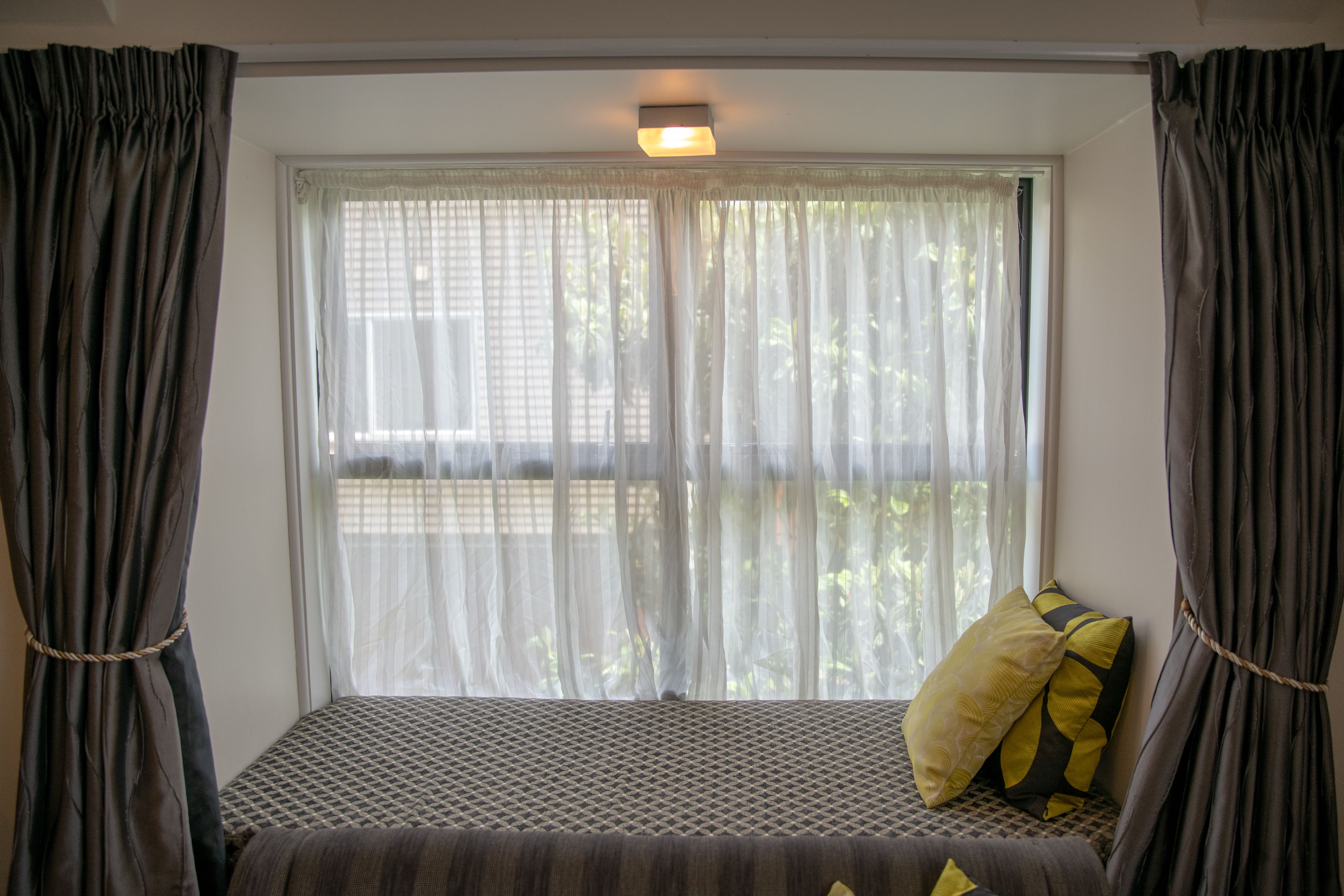 Een kamer met een bed, een raam met dunne gordijnen en uitzicht op groen.