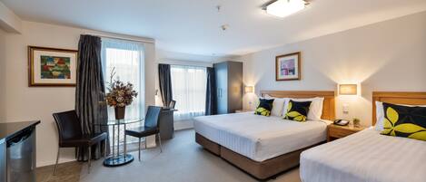 A hotel room with two beds, a desk, a chair, and a small table with a vase.