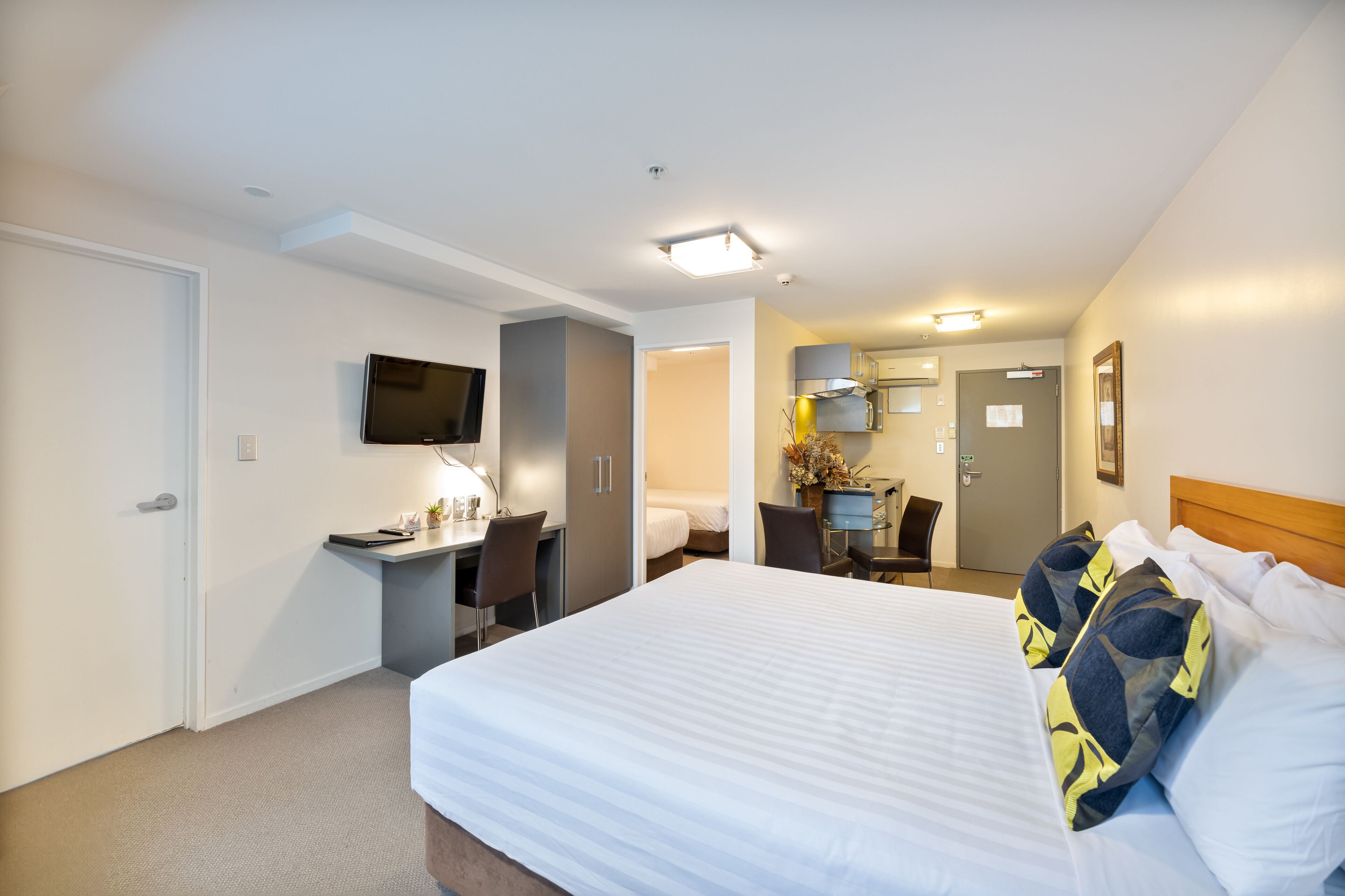 A hotel room with a large bed, a desk with a chair, a television, and a bathroom visible through an open door.