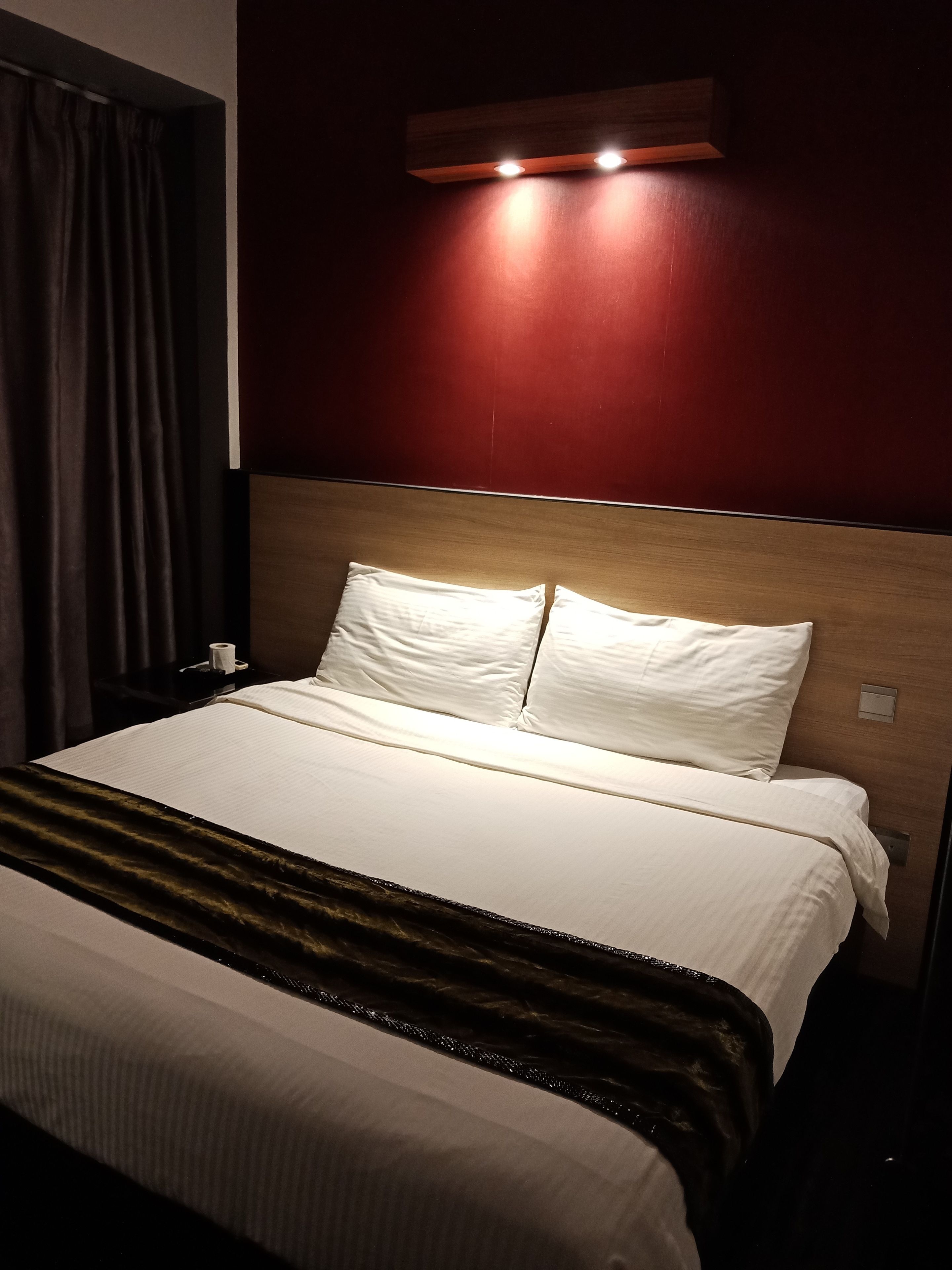 A hotel room with a large bed, a wooden headboard, and a wall-mounted light fixture.