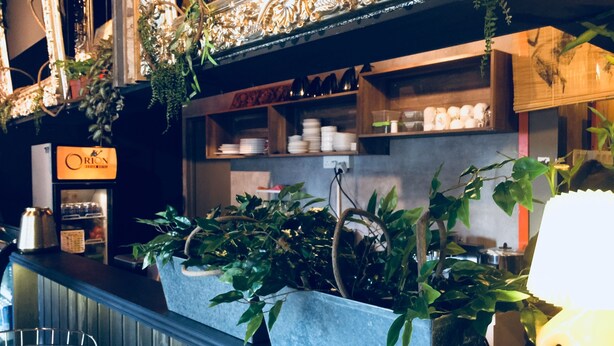 Un área de bar con mostrador, estantes con platos y vasos, y un refrigerador con la etiqueta 'Orion'.