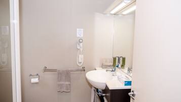 Une salle de bain comprenant des toilettes, un lavabo, un miroir, un porte-serviettes et un sèche-cheveux.