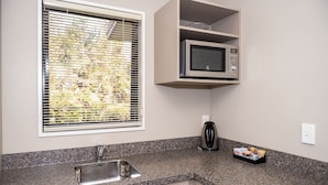 A kitchen with a granite countertop, a stainless steel sink, a microwave, and a kettle. - 58 On Cron Motel (Franz Josef Glacier)