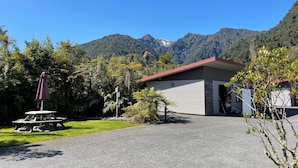 A building with a red roof and stone facade, surrounded by lush greenery and mountains in the background. - 58 On Cron Motel (Franz Josef Glacier)