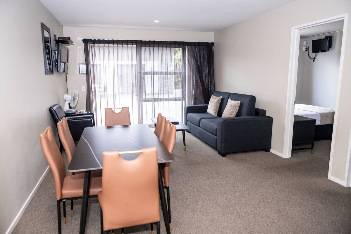 A modern living room with a dining table and chairs, a sofa, a TV, and a small kitchenette.