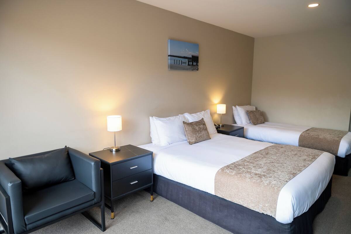 A hotel room with two beds, a sofa, bedside tables with lamps, and a painting on the wall.
