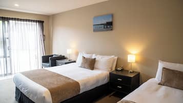 A hotel room with a large bed, a desk, two bedside lamps, and a window with sheer curtains.