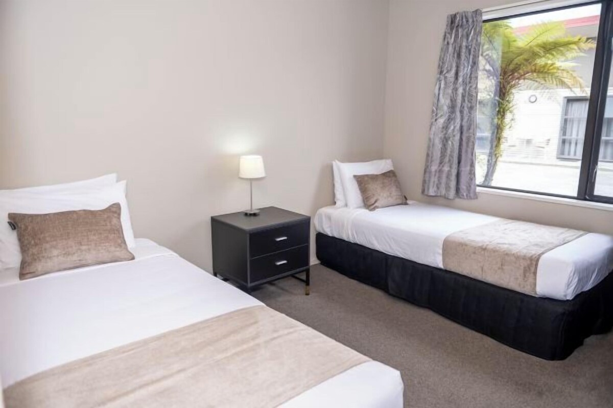 A hotel room with two beds, a nightstand, and a window with curtains.