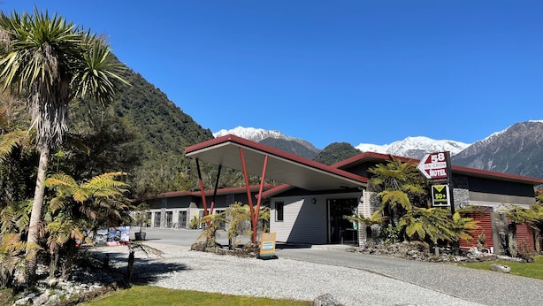 A motel with a red roof, located in a mountainous area with a clear sky. - 58 On Cron Motel (Franz Josef Glacier)