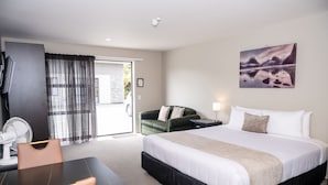 A hotel room with a bed, a desk, a chair, a fan, a green sofa, and a painting on the wall. - 58 On Cron Motel (Franz Josef Glacier)