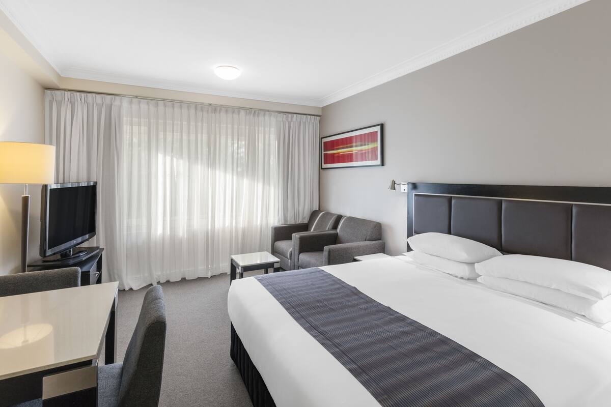 A hotel room with a large bed, a TV, a desk, and a chair.