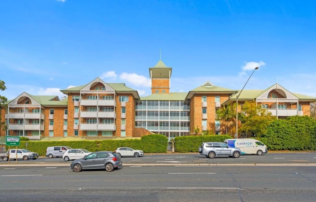 A multi-story hotel with a central tower, a parking lot with several cars, and a clear blue sky.