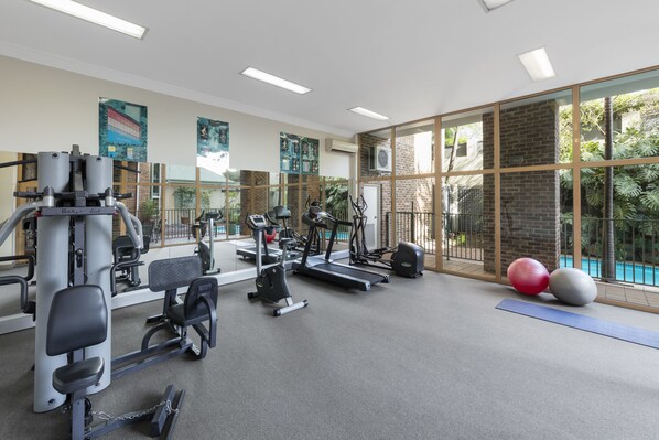 A gym with various exercise equipment, large windows, and a view of a swimming pool. - Nesuto Pennant Hills (Pennant Hills)