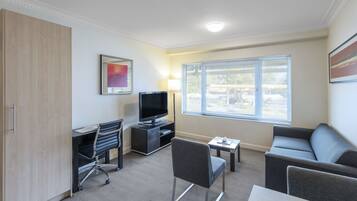 Une chambre d’hôtel moderne équipée d’une télévision à écran plat, d’un canapé, d’un bureau avec une chaise, d’une lampe et d’une fenêtre avec des stores.
