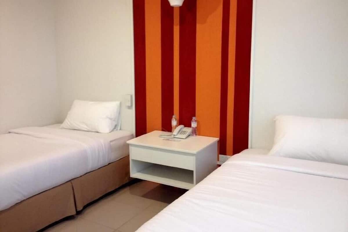 A hotel room with two single beds, a small bedside table with a phone and water bottle, and a wall-mounted light fixture.