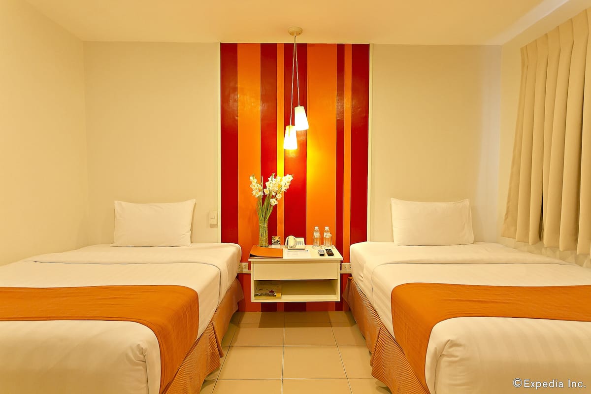 A hotel room with two beds, a nightstand, a vase with flowers, and a striped wall.