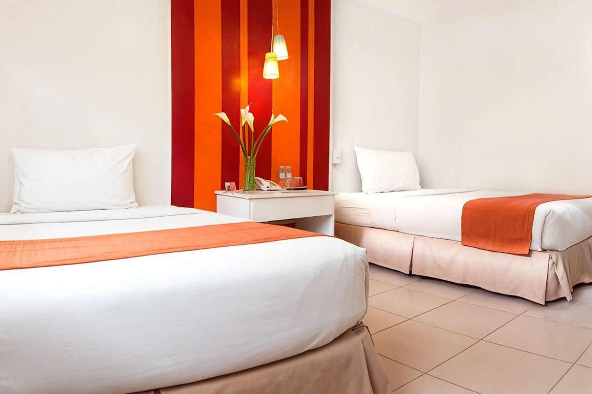 Une chambre d’hôtel avec deux lits, une table de chevet, un vase avec des fleurs et un téléphone.