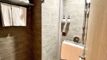 Casa de banho moderna com cabine de duche em vidro, um porta-toalhas com toalhas dobradas e um dispensador de sabonete visível.
