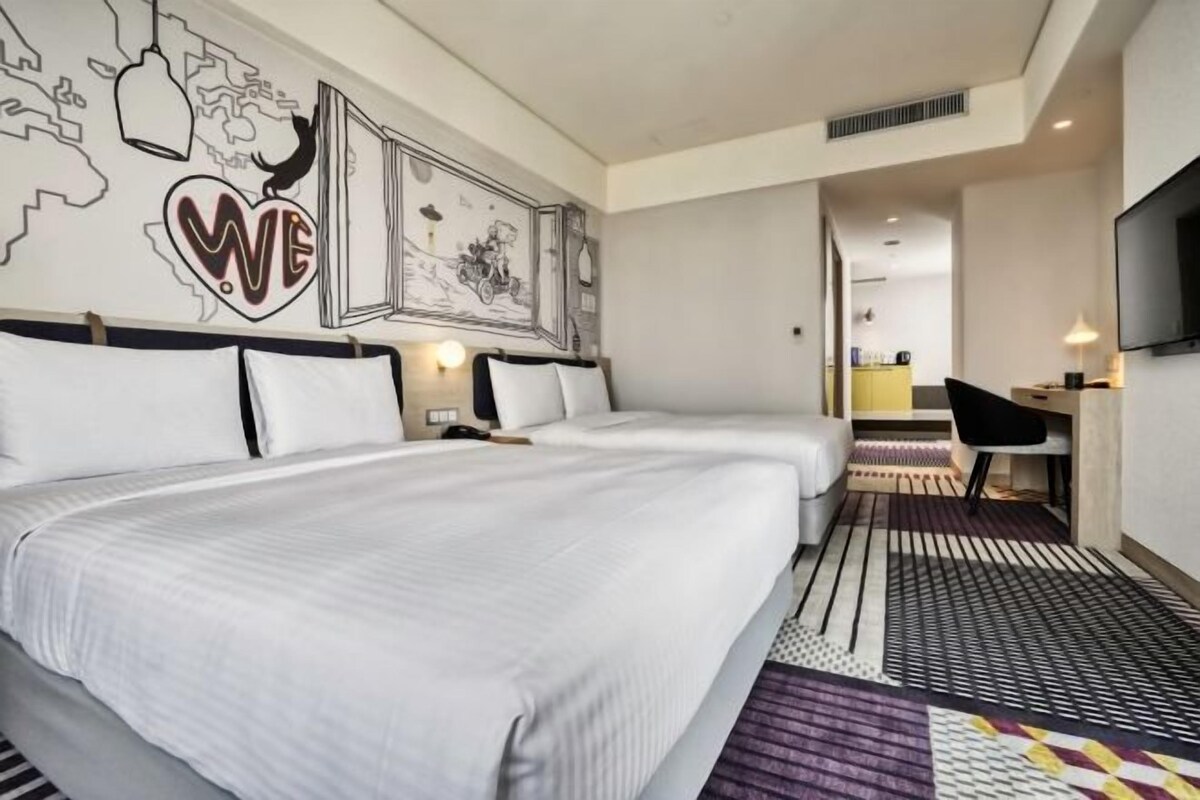 A hotel room with two beds, a desk, a TV, and a world map on the wall.