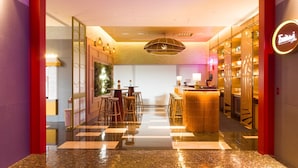 A modern hotel lobby with a bar area, a reception desk, and a seating area with bar stools.