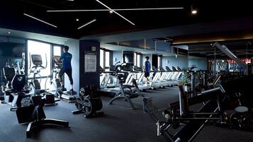 Academia com esteiras, aparelhos de musculação e uma pessoa usando uma bicicleta ergométrica.