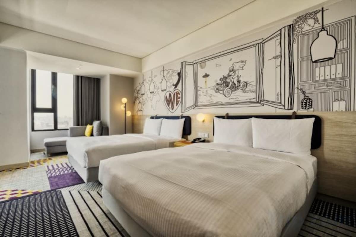 A hotel room with two beds, a large window, and a wall with a mural.