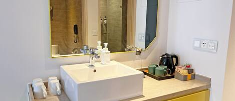 A modern bathroom with a large mirror, white sink, yellow cabinets, and a coffee maker on the counter.