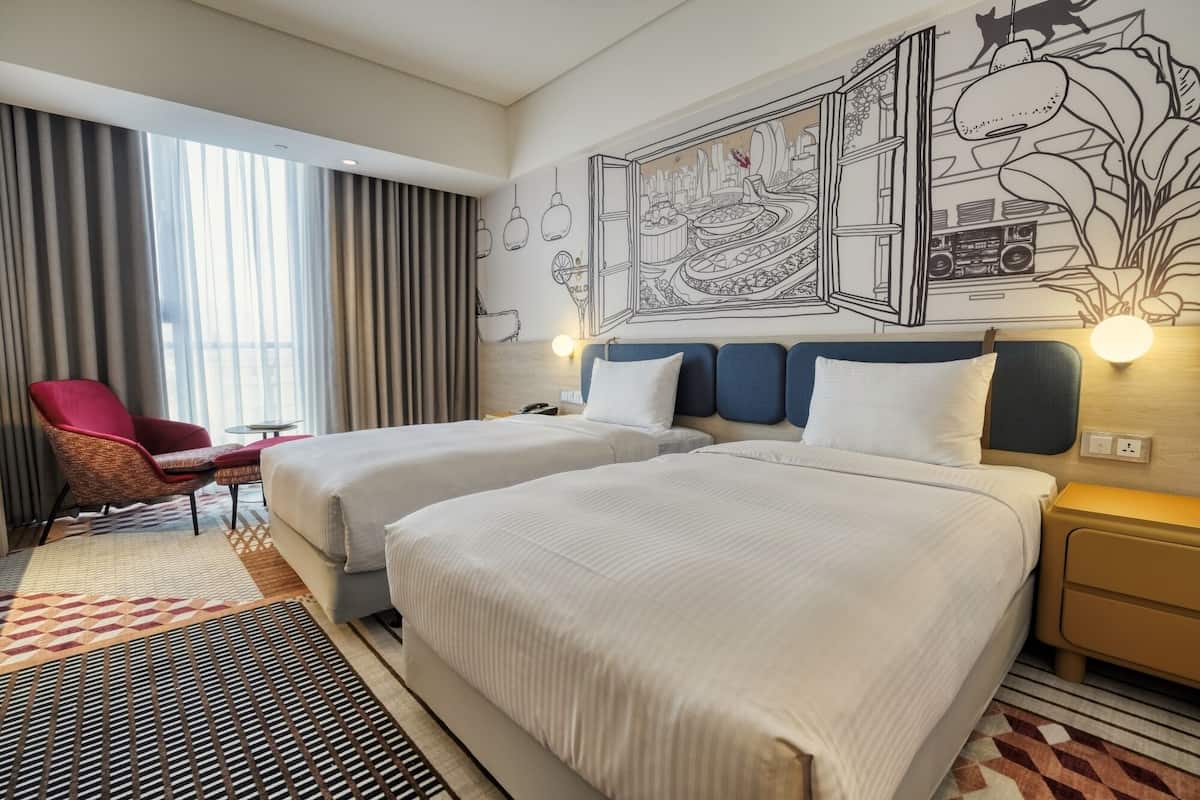 A hotel room with two beds, a red chair, a small table, and a large wall mural.