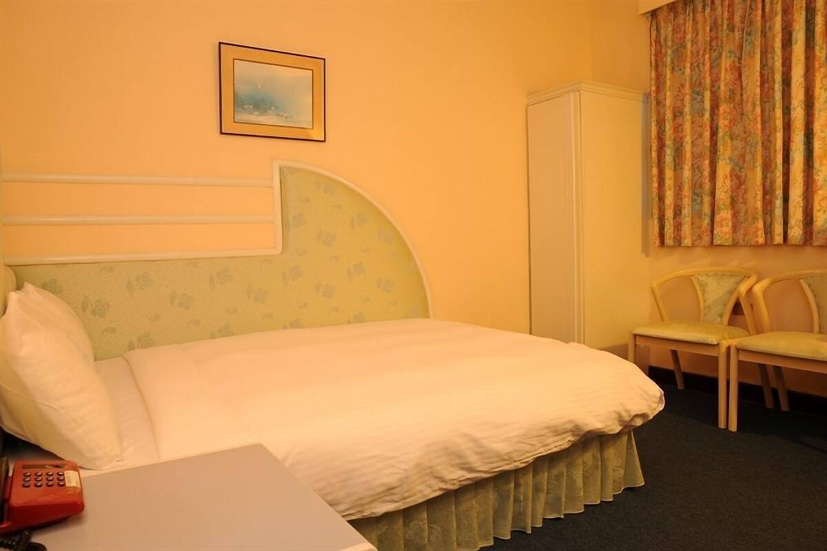 A hotel room with a bed, a telephone, a chair, and a wardrobe.