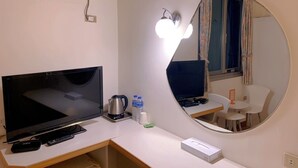 A hotel room with a large flat-screen TV, a coffee maker, two bottles of water, a remote control, a small table with a chair, and a round mirror on the wall. - Traveler Hotel (Taitung)