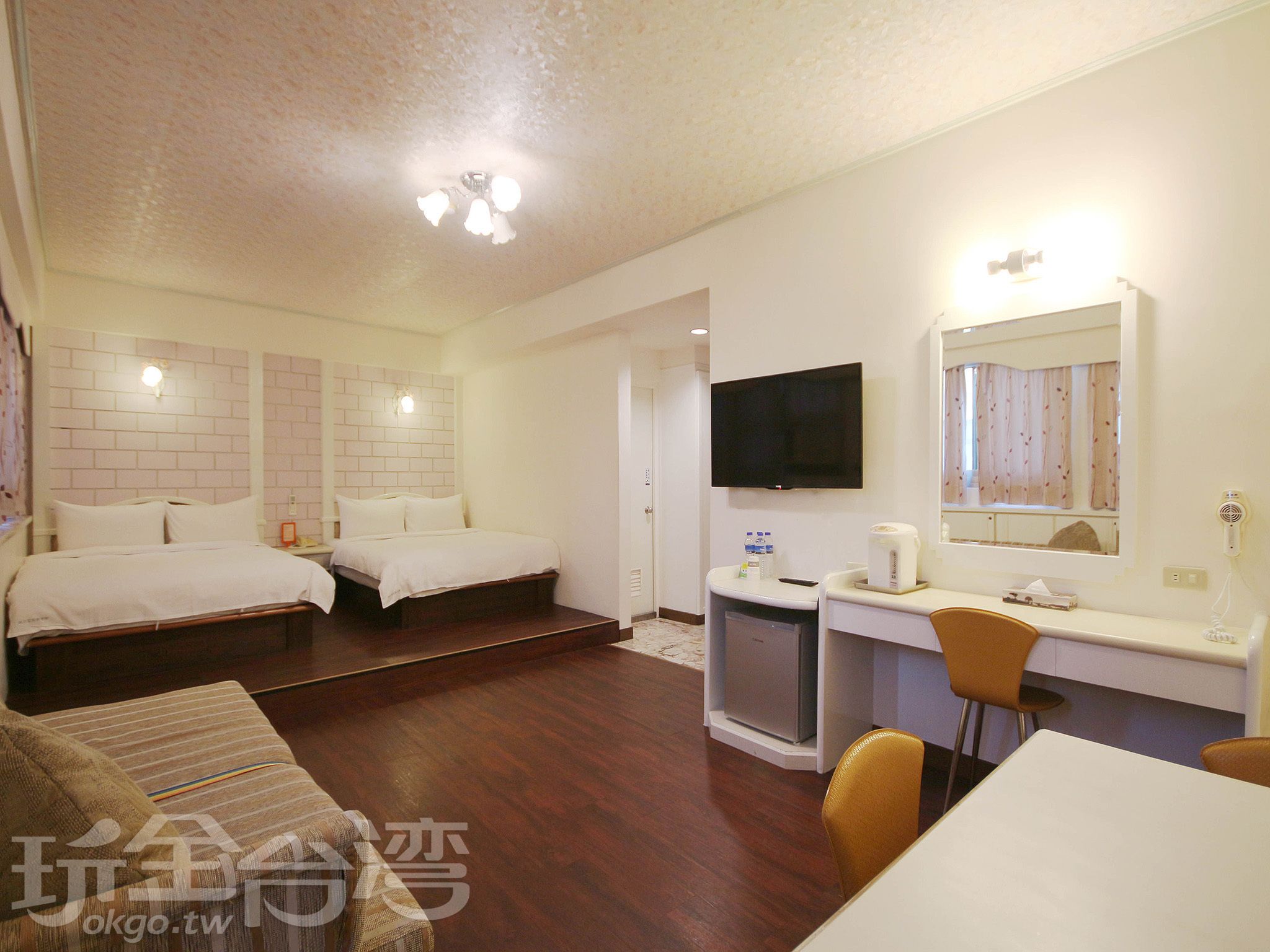 A hotel room with two beds, a desk, a chair, a TV, and a mirror.