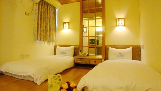 A hotel room with two beds, a wooden ceiling, a window with curtains, and wall-mounted lights. - Traveler Hotel (Taitung)