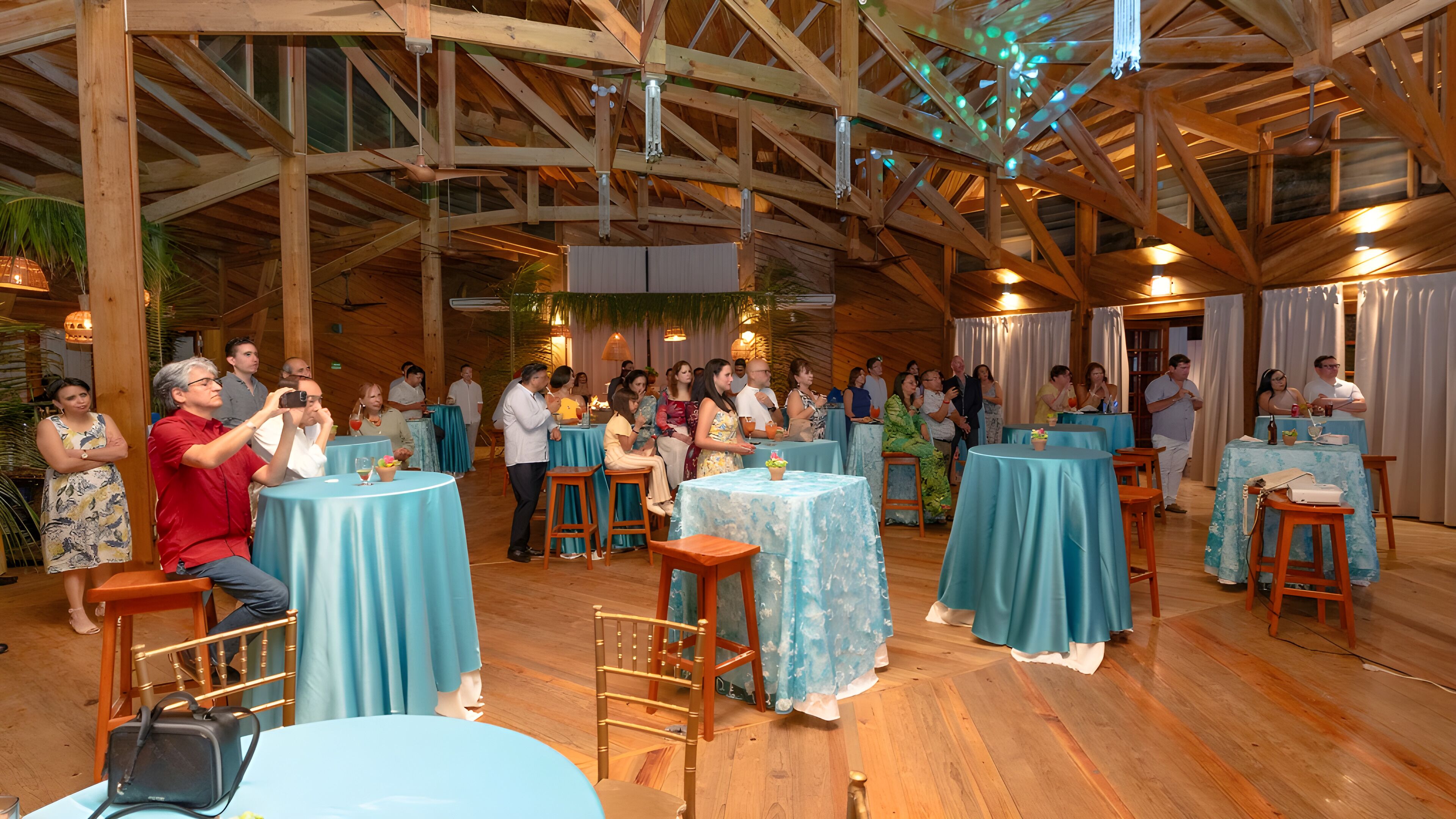 A rustic venue with wooden beams and tables covered with blue tablecloths.