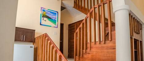 A staircase with wooden railings leading to an upper floor, a white refrigerator, and a painting on the wall.