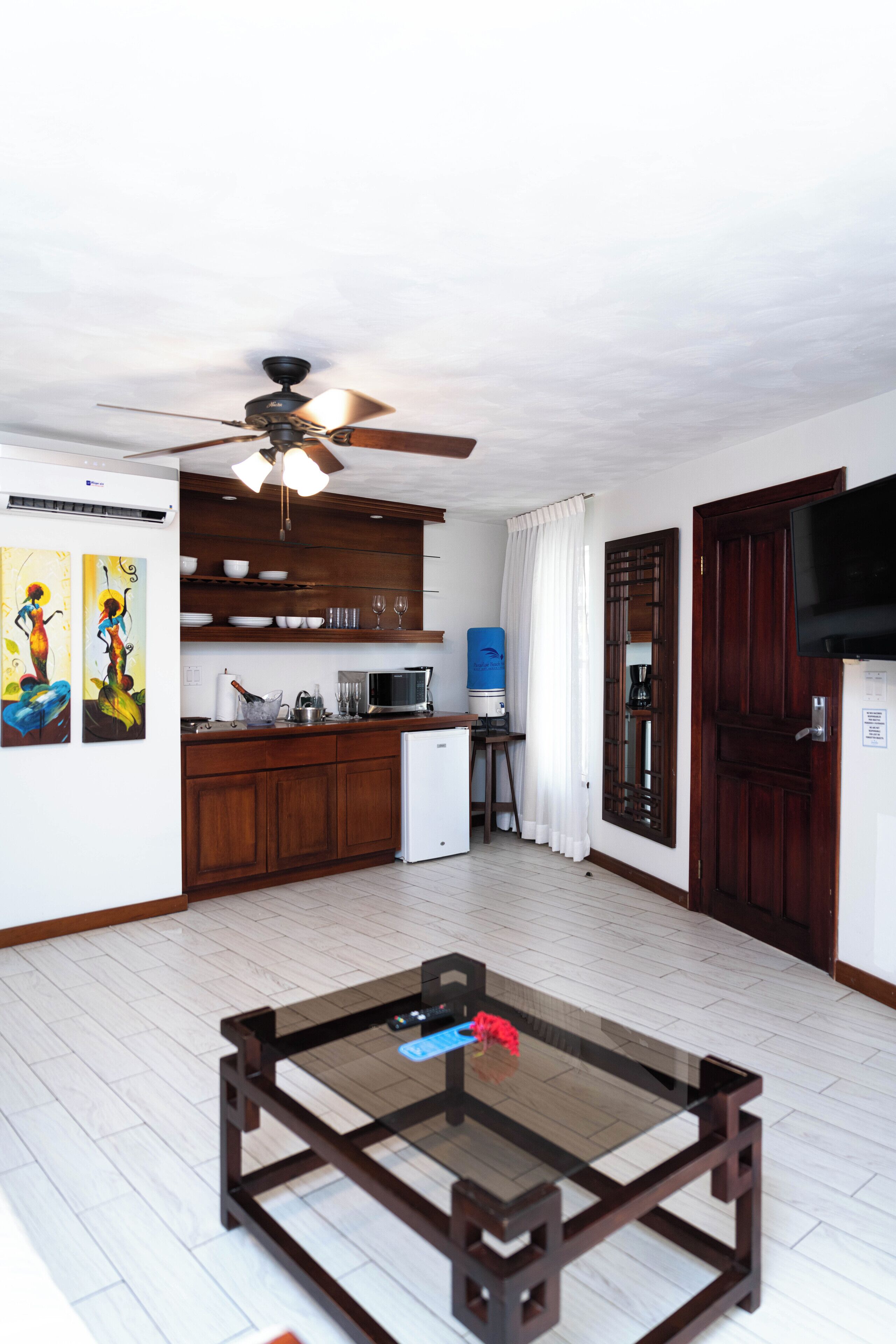 A compact living space with a kitchenette, a ceiling fan, a television, and a glass-top coffee table.