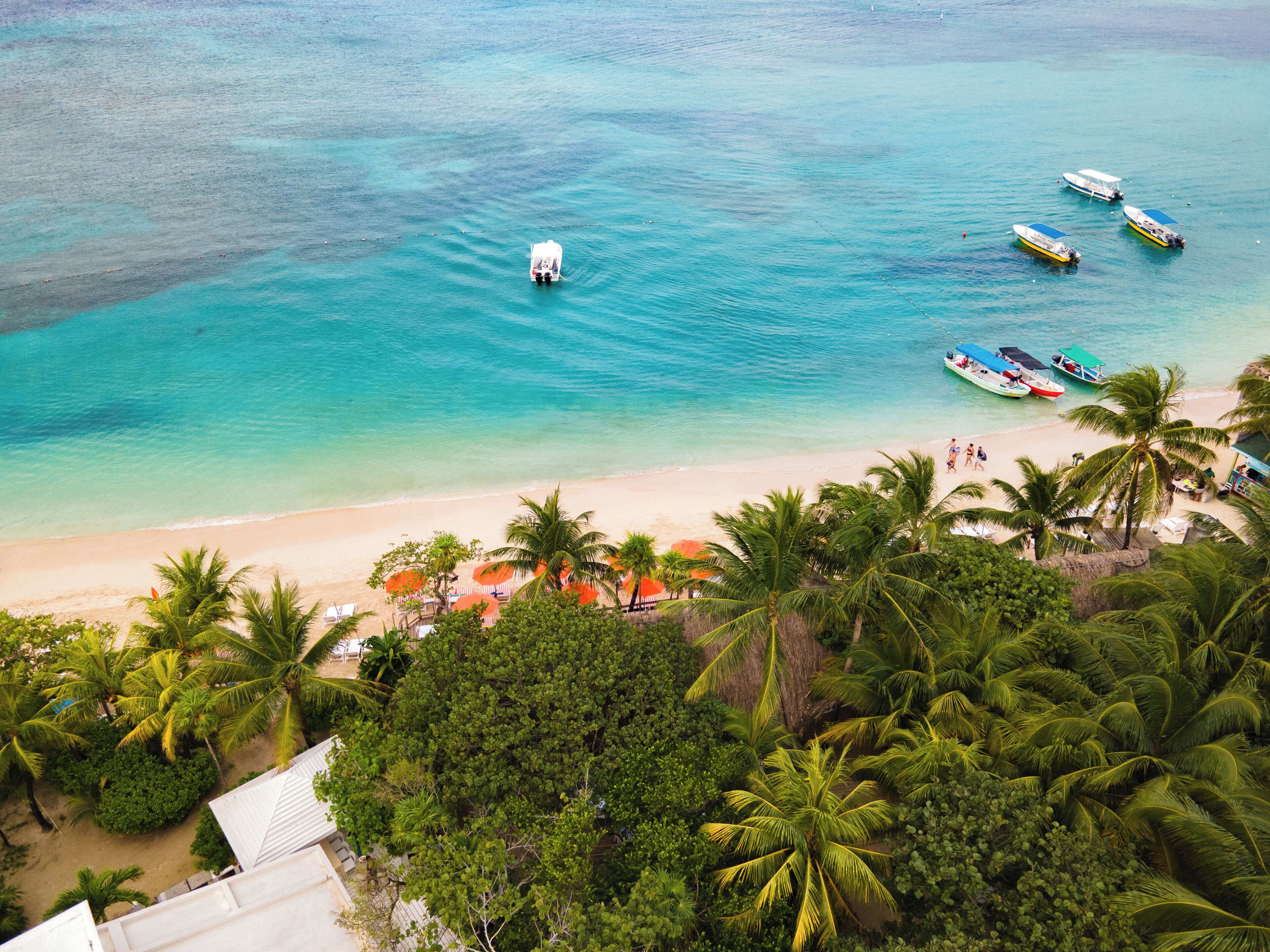 Una playa tropical con aguas turquesas cristalinas, varios barcos y exuberantes palmeras.
