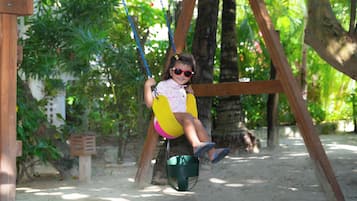 Niño en un columpio en un parque con árboles y un conjunto de columpios de madera.