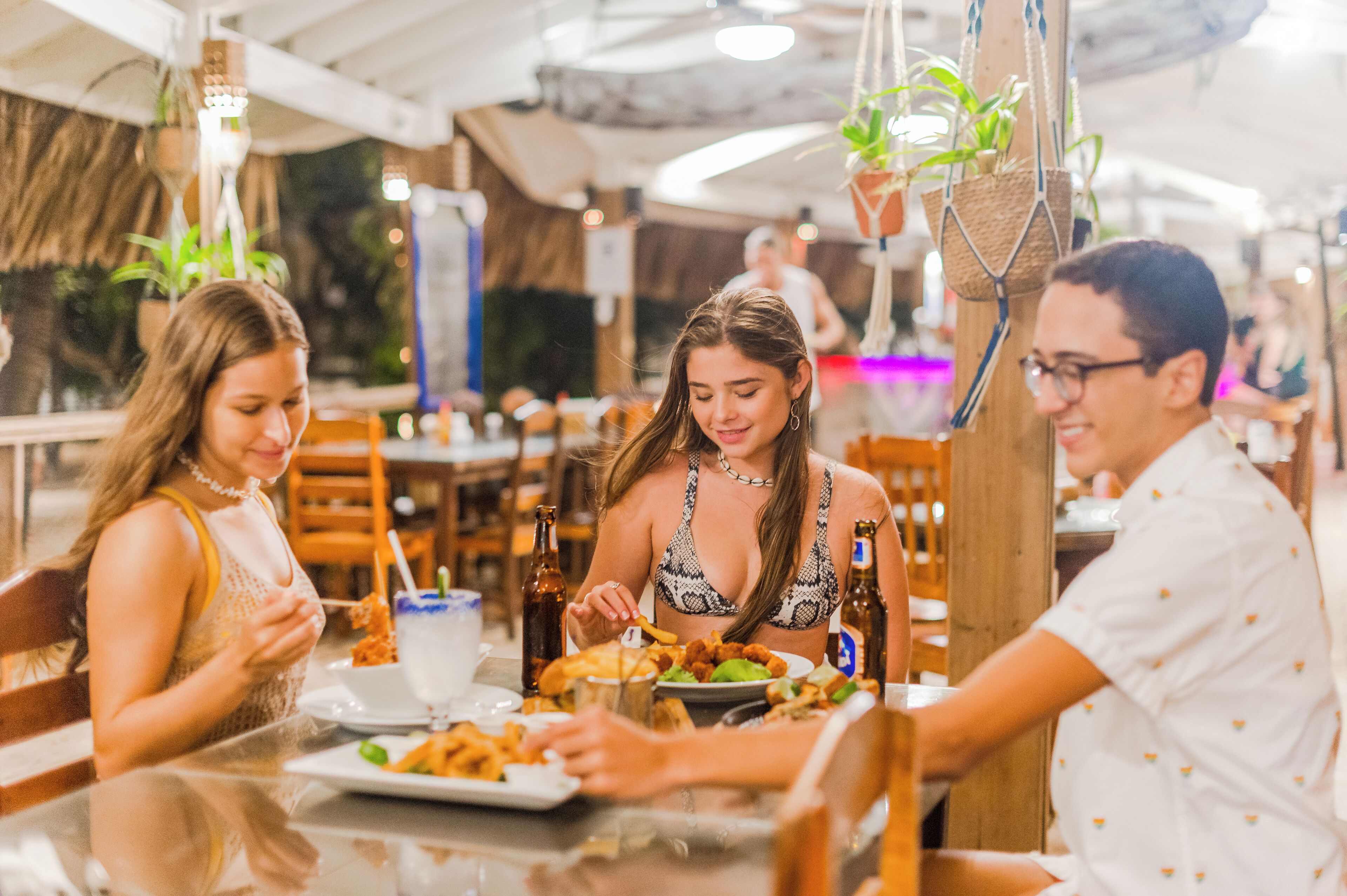 Un restaurante con mesas y sillas de madera, plantas colgantes y un ambiente informal para comer.